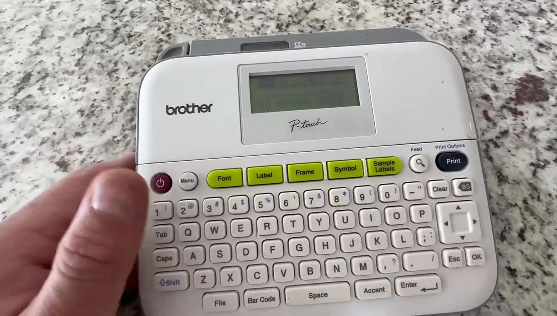 The user interface of the P-Touch PTD210 label maker with the power button and other controls visible.