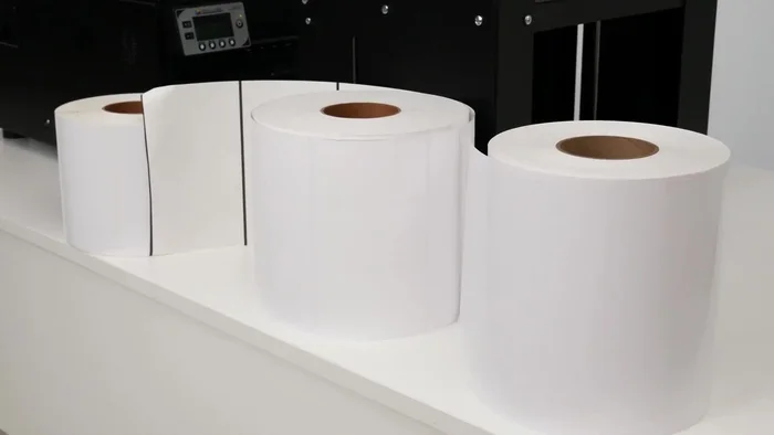 Load the label roll into the printer. Guide the roll under the dancer arm and feed it into the back of the printer.